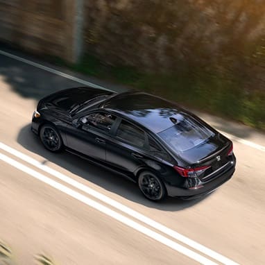 2027 Honda Civic Sedan Sport in Crystal Black Pearl high-angle rear three-quarter view driving on a road (Compact Sedan)